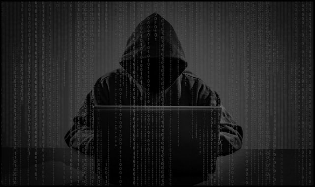 Hacker in black hoodie sitting behind laptop